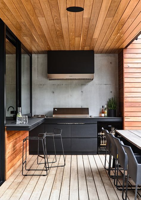 a-contemporary-outdoor-barbecue-area-done-in-black-and-stained-wood-with-matte-cabinets-a-grill-a-hood-and-some-meal-spaces